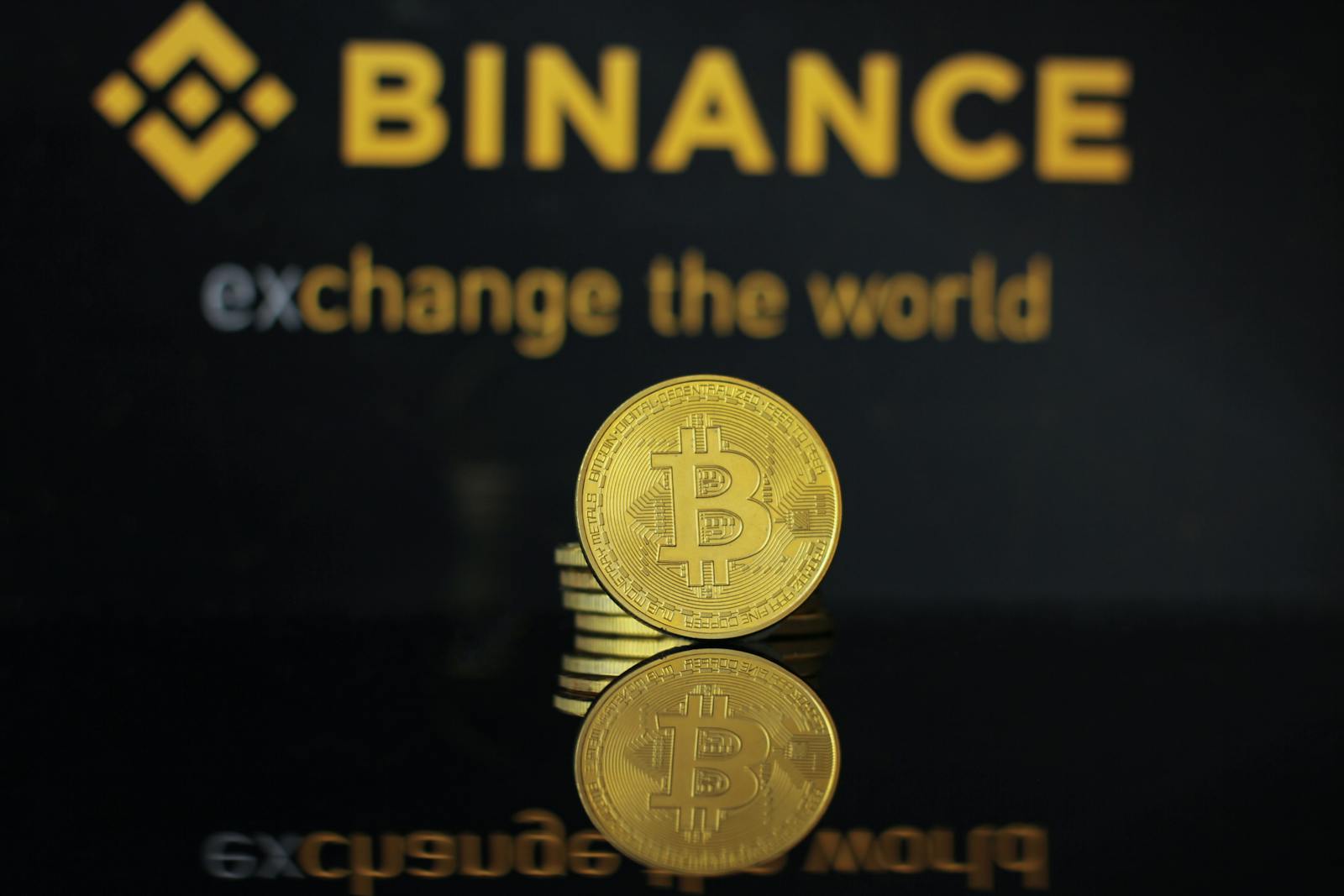 Zbliżenie monety Bitcoin z logo Binance i tekstem odbijającym się w ciemnej powierzchni.
