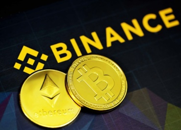 two gold bitcoins sitting next to a binance sign