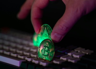 Close-up of a hand placing bitcoin and ethereum coins onto a computer keyboard, symbolizing cryptocurrency and digital finance.