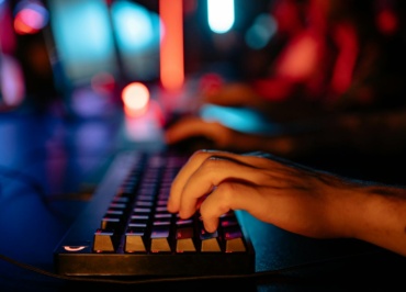 Fingers typing on an illuminated keyboard in a dimly lit room, creating a tech-focused atmosphere.