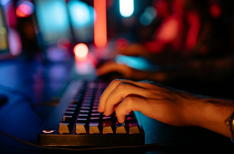 Fingers typing on an illuminated keyboard in a dimly lit room, creating a tech-focused atmosphere.