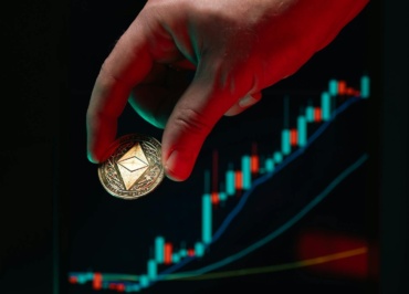 A hand holding an Ethereum coin against a rising stock market graph, symbolizing cryptocurrency growth.
