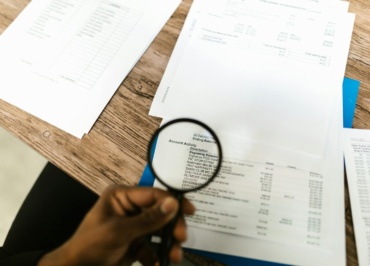 Close-up of hand using magnifying glass to review documents. Ideal for financial themes.