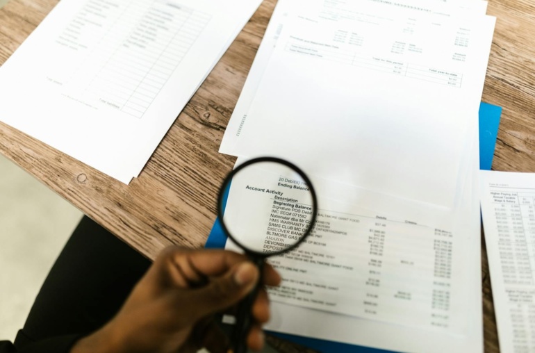 Close-up of hand using magnifying glass to review documents. Ideal for financial themes.