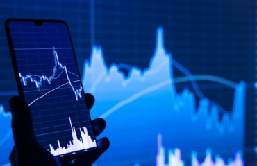 a person holding a cell phone in front of a stock chart