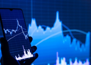 a person holding a cell phone in front of a stock chart