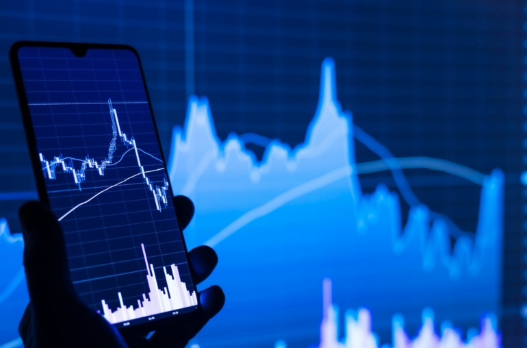 a person holding a cell phone in front of a stock chart